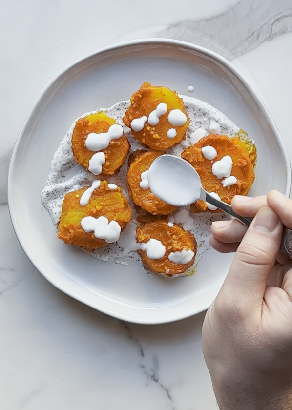 potatoes being doused in a creamy yogurt sauce